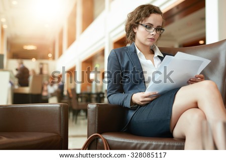 Portrait of busy young woman reading contract documents. Businesswoman sitting at cafe going through business reports.