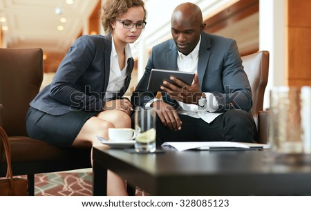 Business people discussing business ideas looking at digital tablet. Young man and woman working on tablet computer while sitting at hotel lobby.