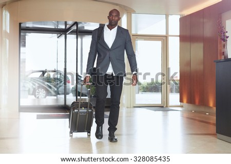 Businessman walking in hotel lobby. Full length portrait of young african executive with a suitcase.