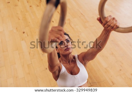 Determined young woman at gym. Muscular female athlete working out using gymnastic rings.