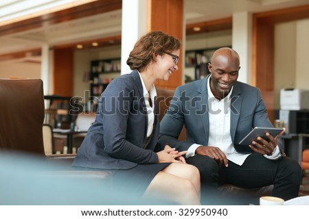 Shot of two people looking at something on a touchscreen computer. Smiling business people using digital tablet while sitting at coffee shop.