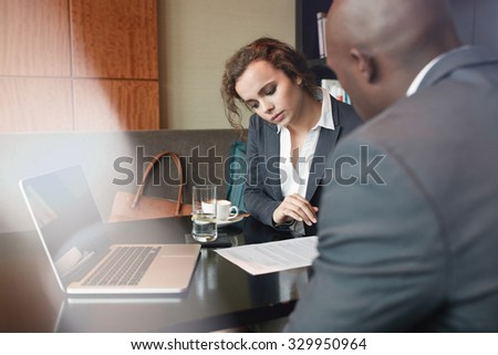 Serious business people working together in a cafe and reading some contract documents. Businessman and businesswoman discussing paperwork at table.