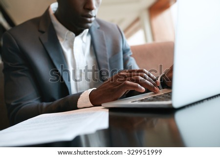 Close up shot of male hands typing on laptop keyboard. African businessman working on laptop computer at cafe.
