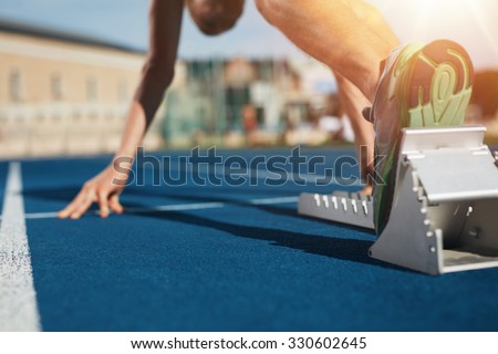 Feet on starting block ready for a spring start.  Focus on leg of a athlete about to start a race in stadium with sun flare.