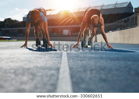 Sprinters at starting blocks ready for race . Athletes at starting position on athletics stadium race track with sun flare.