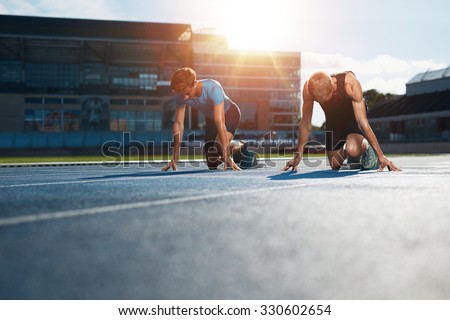 Young athletes preparing to race in start blocks in stadium. Sprinters at starting blocks ready for race with sun flare.