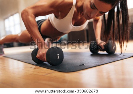 Muscular woman doing push-ups on dumbbells in gym. Powerful female exercising in health club.