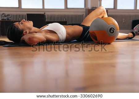 Image of young woman relaxing on exercise mat after intense workout at gym. Fit female athlete lying on floor.