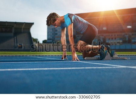 Young athlete at starting position ready to start a race. Male runner ready for sports exercise on racetrack with sun flare.