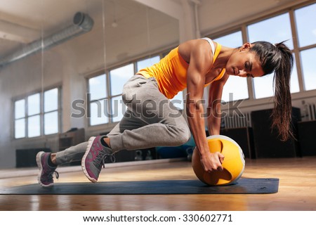 Fit female doing intense core workout in gym. Young muscular woman doing core exercise on fitness mat in health club.