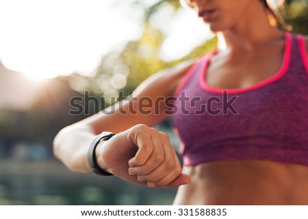 Young fitness woman looking at her smart watch while taking a break from sports training. Sportswoman checking pulse on fitness smart watch device.