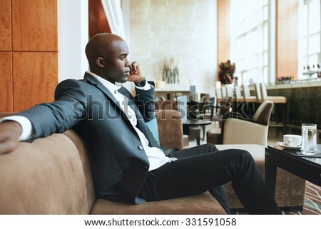 Young businessman sitting relaxed on sofa at hotel lobby making a phone call, waiting for someone.