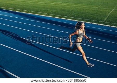 Young woman running on racetrack during training session. Female runner practicing on athletics race track.