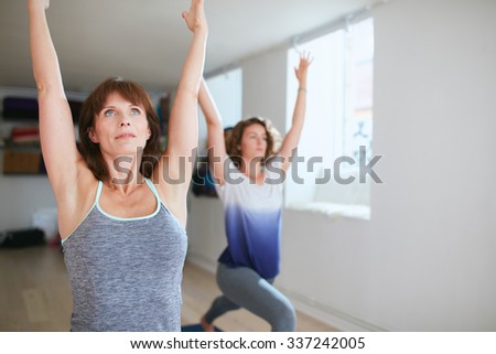 Two women practicing yoga forms and positions in gym. Fitness females doing warrior pose at yoga class. Virabhadrasana posture in training session.