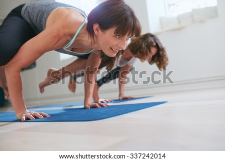 Two women at yoga class doing yoga hand stand pose. Mature woman standing on hands with feet lifted up doing crane yoga pose - Bakasana.