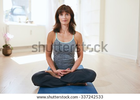 Shot of an attractive young woman meditating on an exercise mat. Fit female sitting in meditation pose at fitness club looking at camera. She is doing Padmasana.