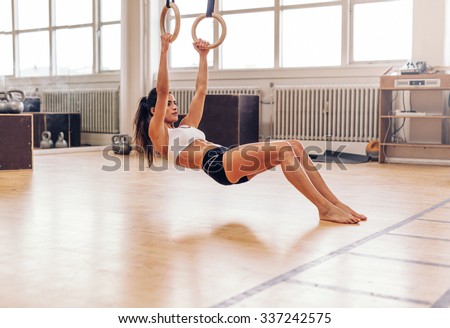 Muscular young woman doing pull-ups on rings. Fit young female athlete exercising with gymnastic rings at gym.