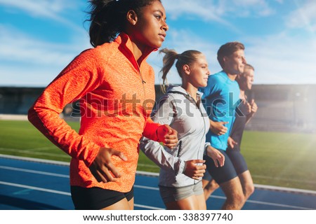 Young african woman running with her team on running track in stadium. Multiracial team of runner practicing at athletics stadium on a sunny day.