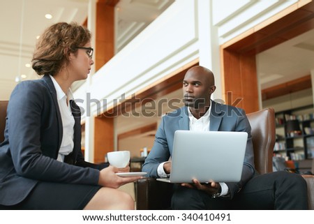 Two businesspeople having meeting in cafe. Businessman with laptop and businesswoman drinking coffee while working in a hotel lobby.