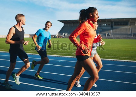 Fit men and women running on a race track. Multiracial athletes practicing on race track in stadium.