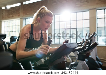 Fit woman working out on exercise bike at the gym. Indoor shot of a female doing fitness training on spinning bicycle at health club.