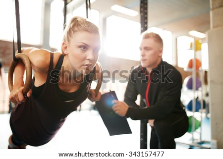 Fit young woman with her personal fitness trainer in the gym exercising with gymnastic rings