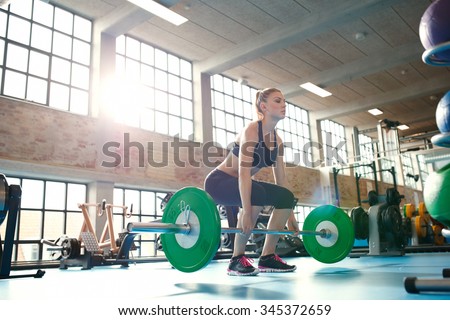 Young woman working hard in the gym. Fit female athlete lifting weights in health club.