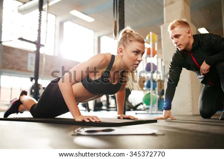 Fitness woman exercising with fitness trainer in gym. Woman doing push ups exercise with her personal trainer at health club.