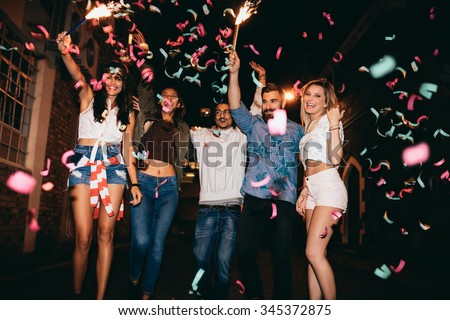 Group of young people having a party, outdoors. Multiracial young men and women celebrating with confetti. Best friend having party at night.