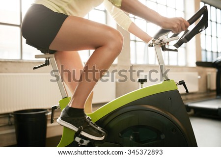Cropped shot of fitness woman working out on exercise bike at the gym. Female exercising on bicycle in health club, focus on legs.