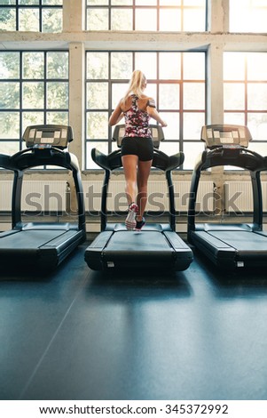Rear view of young female running on treadmill in gym. Fitness woman jogging indoors in health club