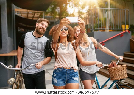 Young african woman taking a self portrait with her friends. African woman taking selfie with mobile phone. Young friends with bikes having fun on city street.