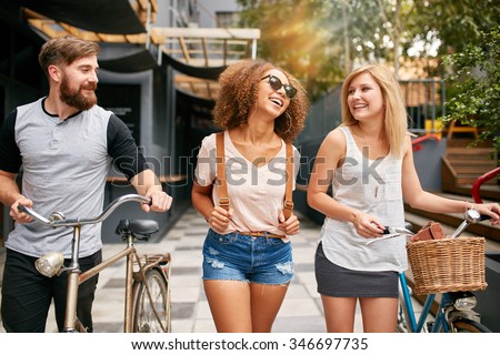 Happy young people walking down the city street with their bicycles and smiling. Young man and women on road with their bikes.