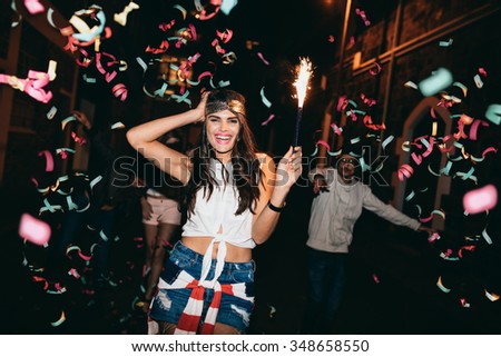 Happy young woman partying with her friends outdoors at night. Friends partying outdoors with confetti and sparklers.