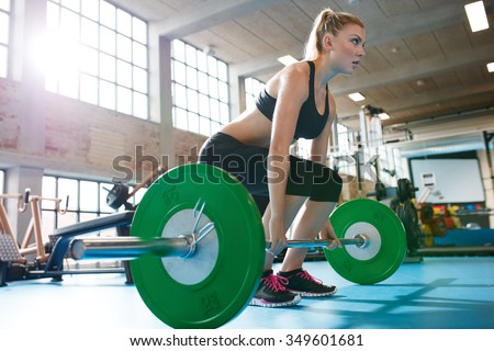 Muscular caucasian woman in a gym doing heavy weight exercises. Young woman doing weight lifting at health club.