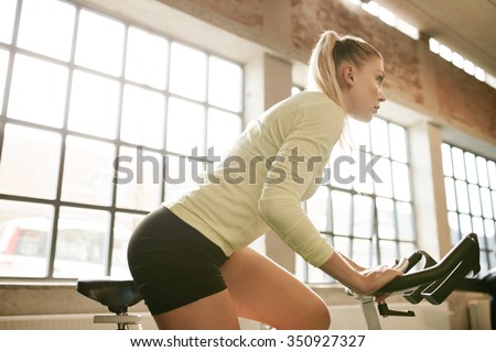 Indoor shot of fit young woman working out on a stationary bike in gym. Determined caucasian female training on exercise equipment in health club.