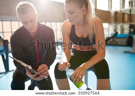 Shot of a personal trainer helping a gym member with her exercise plan. Trainer goes through fitness plan with client in the health club.