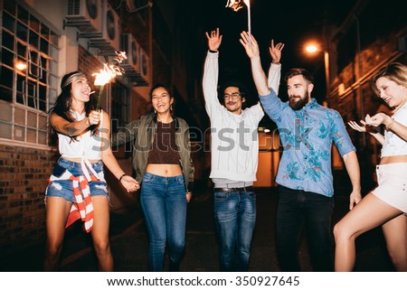 Portrait of happy young friends celebrating new years eve with sparklers at night. Best friends hanging out at night and celebrating 4th of july outdoors.
