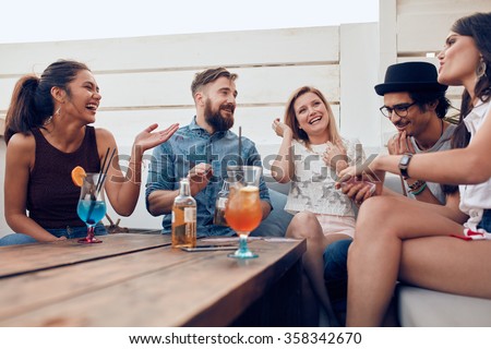 Portrait of happy young people sitting together and laughing. Multiracial friends enjoying at a party with cocktails on table.