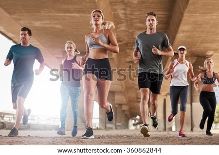 Determined  group of young people running together in city. Low angle shot of running club members training together in morning under a bridge.