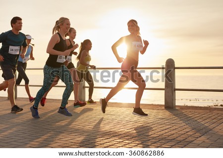 Fit young people running on street by the sea. Runners competing in a marathon race in evening.