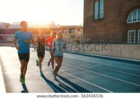 Professional runners running on a race track. Multiracial athletes practicing on race track in stadium on a bright sunny day.