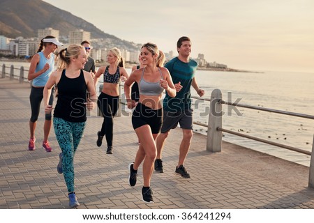 Portrait of young runners enjoying workout on the sea front path along the shoreline.  Running club group running along a seaside promenade.