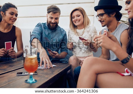Group of friends relaxing and playing cards together. Young people hanging out together around a table during a party playing a game of cards.