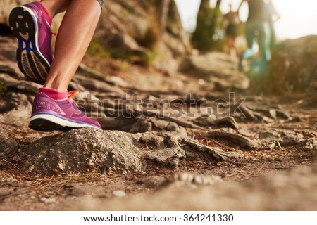 Close up of an athlete\'s feet wearing sports shoes on a challenging dirt track. Trail running workout on rocky terrain outdoors.