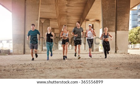Portrait of group of runners from running club under a bridge. Young men and women jogging together.