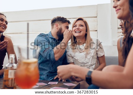 Young people sitting together in a party. Man whispering something in woman\'s ears. Sharing a secret.