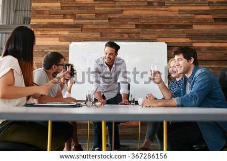 Group of happy young people having a business meeting. Creative people sitting at table in boardroom with man explaining business strategy.