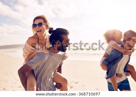 Happy young men giving piggyback ride to women on beach. Diverse group of young people having fun on the beach and piggybacking.