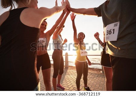 Shot of male and female runners high fiving each other after a race. Diverse group of athletes giving each other high five after winning competition.